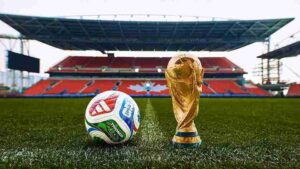 The official Trionda football and the FIFA World Cup trophy rest on the grass of a massive host stadium.