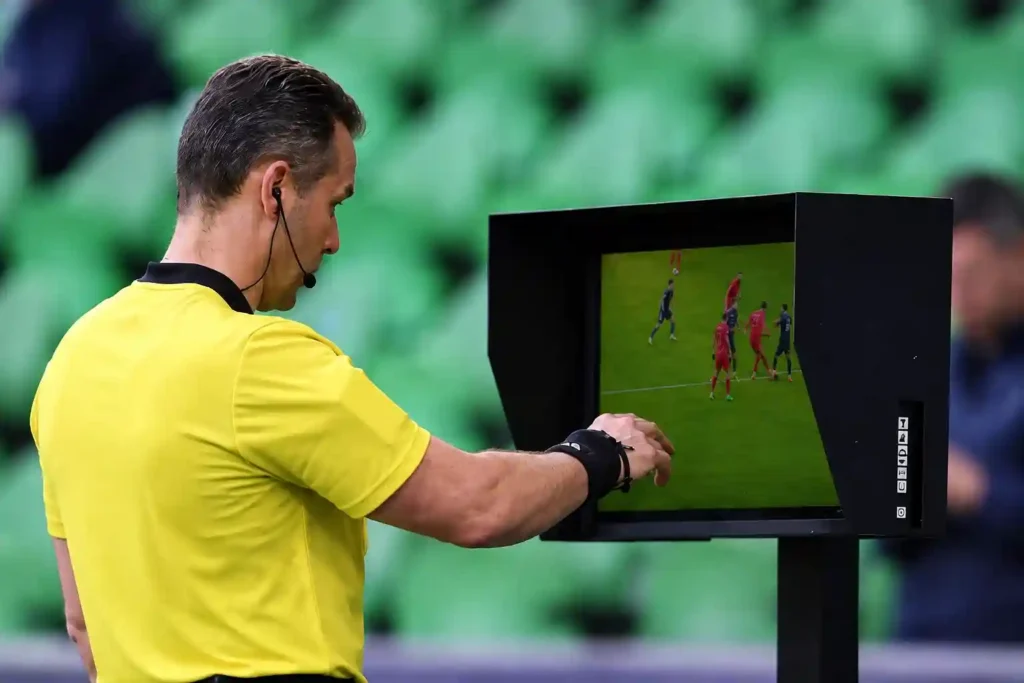 Football referee reviewing a VAR decision on the pitchside monitor